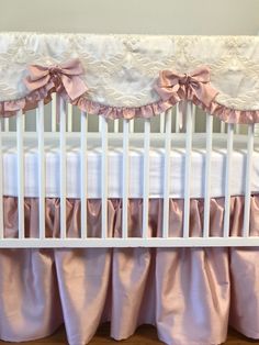 a white crib with pink ruffled bedspread and bows on the bed skirt