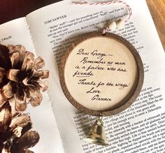 a wooden ornament sitting on top of an open book next to a pine cone