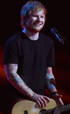 a man with tattoos on his arm and holding a guitar in front of a microphone