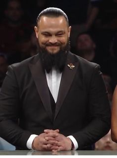 a man in a tuxedo is sitting at a table with his hands folded