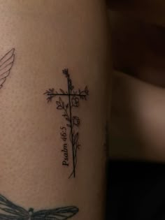 a cross and a dragonfly tattoo on the leg, with words written in cursive writing