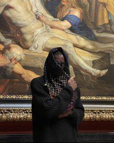 a woman wearing a veil standing in front of a painting with her head covered up