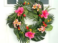 a wreath with pink flowers and green leaves hanging on a white front door, next to a window