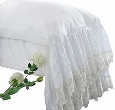 a white bed with lace and flowers on the bottom layer, next to it is a pillow