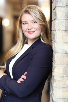 a woman standing next to a brick wall with her arms crossed and looking at the camera