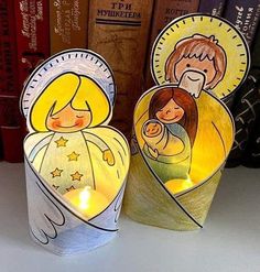 two paper cupcakes with candles in the shape of an angel and a baby jesus