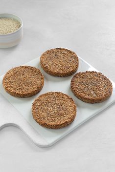 four cookies on a white tray next to a bowl of oatmeal