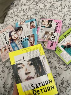 a person is holding several books in their hand on a bed with floral print sheets