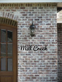 a brick wall with the words mill creek written on it and a lantern hanging from the side