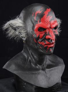 a man with red paint on his face and hair is wearing a black mask that looks like a demon