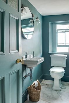 a bathroom with blue walls and a white toilet next to a sink under a mirror