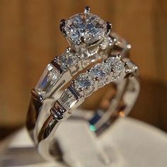 two wedding rings with diamonds on them sitting on top of a white cloth covered table