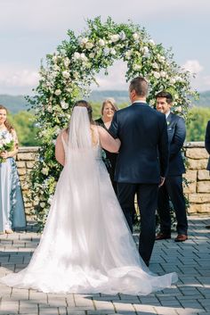 a bride and groom walking down the aisle at their wedding ceremony in front of an arch with white flowers