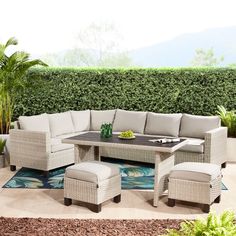 an outdoor patio furniture set with beige cushions and matching foot stools, in front of a green hedge