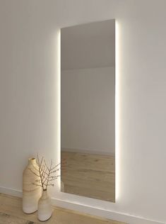 a white vase sitting on top of a hard wood floor next to a large mirror