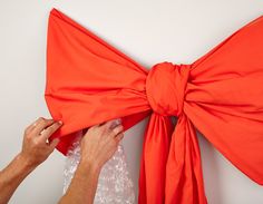 someone is tying the back of an orange bow to a wall hanging on a white wall