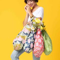 a woman carrying two large bags with flowers in them and smiling while standing against a yellow background