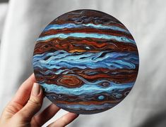 a hand holding up a painted disc with the planet in it's outer half