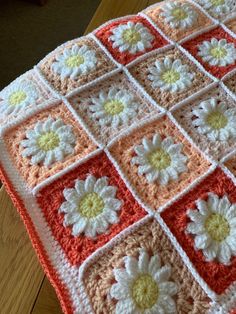 a crocheted blanket with white and yellow flowers on the edges is sitting on a wooden table