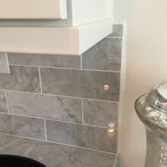 a bathroom with grey marble tile and white counter tops, along with a black trash can