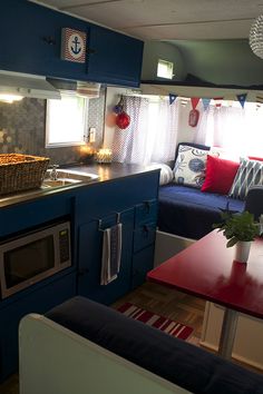 a kitchen and living room inside of a small house with blue cabinets, red counter tops, and white curtains