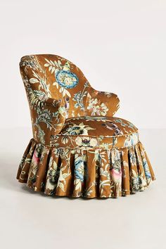 an upholstered chair with a flowered pattern on the back and pleated skirt