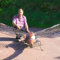 a man sitting on the ground next to a sculpture of a dragon with two wings