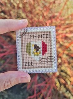 someone is holding up a small cross - stitch card with the word mexico on it