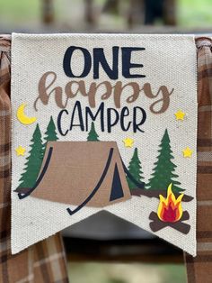 one happy camper banner hanging on a chair with a campfire and tent in the background