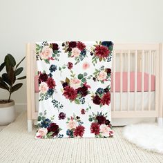 a baby crib with a flowered blanket next to a potted plant on the floor