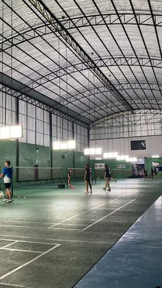 people playing tennis in an indoor court with green walls and metal roofing overhangs