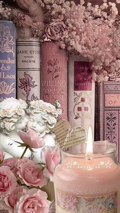 there is a candle and some books on the shelf next to each other with pink flowers