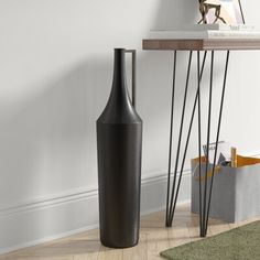 a tall black vase sitting on top of a wooden floor next to a book shelf