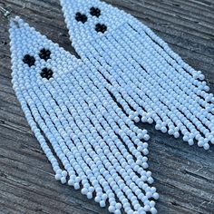 two white beads with black eyes are hanging on a wooden surface, one is shaped like a ghost