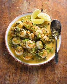 a white bowl filled with shrimp and broccoli next to a spoon on top of a wooden table