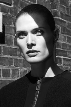 a woman standing in front of a brick wall wearing a black top and silver necklace