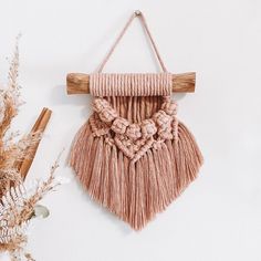 a wall hanging made out of yarn and wooden dows on a white wall next to dried flowers