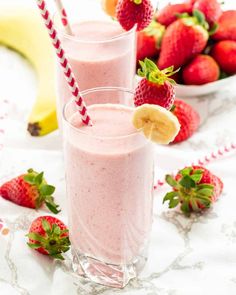 two glasses filled with smoothie next to bananas and strawberries on a tablecloth