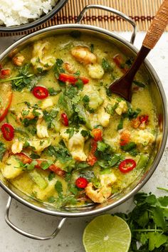 a pan filled with shrimp and vegetables on top of a table next to rice, lime wedges and cilantro