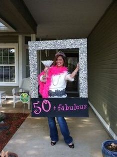 a woman holding a sign that says 50 fabulous and standing in front of her house