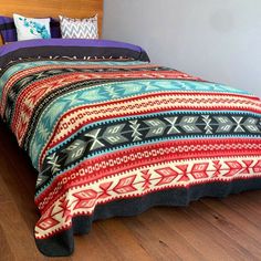 a bed with colorful blankets and pillows on top of it in a room that has hardwood floors