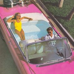 a man and woman riding in the back of a pink car