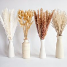 three white vases with dried plants in them