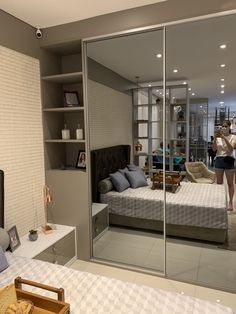 a woman is standing in front of a mirrored closet door and looking into the bedroom