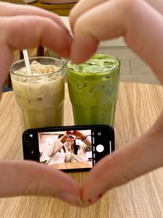 two people are making a heart shape with their hands while holding up a cell phone