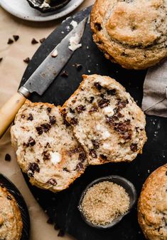 chocolate chip muffins on a black cutting board next to some butter and sugar