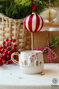 a white coffee cup sitting on top of a table next to christmas decorations and presents