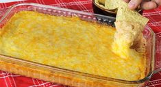 a person dipping a tortilla chip into a casserole dish with cheese