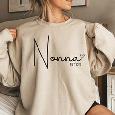 "Introducing our Custom Nonna Sweatshirt, the perfect holiday gift for your beloved Nonna! Made with love and care, this sweatshirt is an ideal Mothers Day gift for nonnas or a heartwarming present for any occasion. Our sweatshirt is comfortable and stylish, featuring a unique design that proudly displays the title \"Nonna.\" Perfect for pregnancy reveals or as a gift from the grandkids, this Nonna shirt is sure to bring a smile to her face. Treat your Nonna to something special and show her how Nonna Gifts, Nana Sweatshirt, Gift From Grandkids, Mama Sweater, Mama Hoodie, Mommy Outfits, New Grandparents, New Grandma, Kids Names