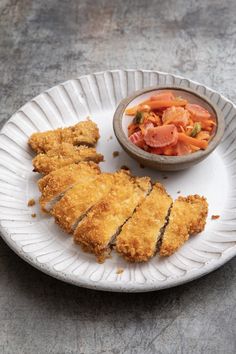 a white paper plate topped with chicken strips next to a bowl of carrots and salad